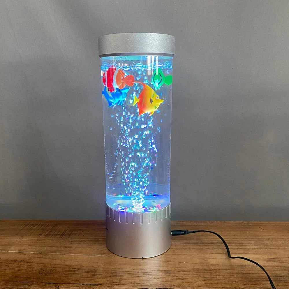 Silver cylindrical bubble lamp with colorful LED-lit artificial fish floating inside on wooden table