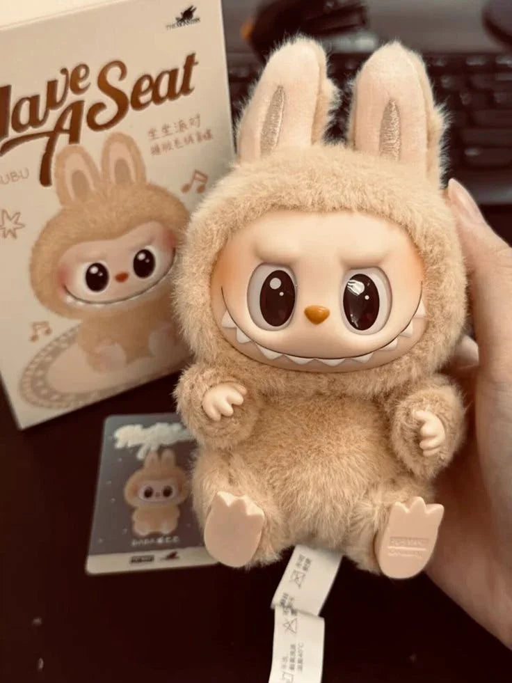 Hand holding a plush Labubu toy with big eyes and bunny ears, box and card in background
