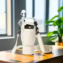 White insulated water bottle with shoulder strap on wooden table near window and plant
