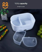 White 1.5L capacity divided lunch box with transparent lid on dark table, surrounded by snacks and grapes