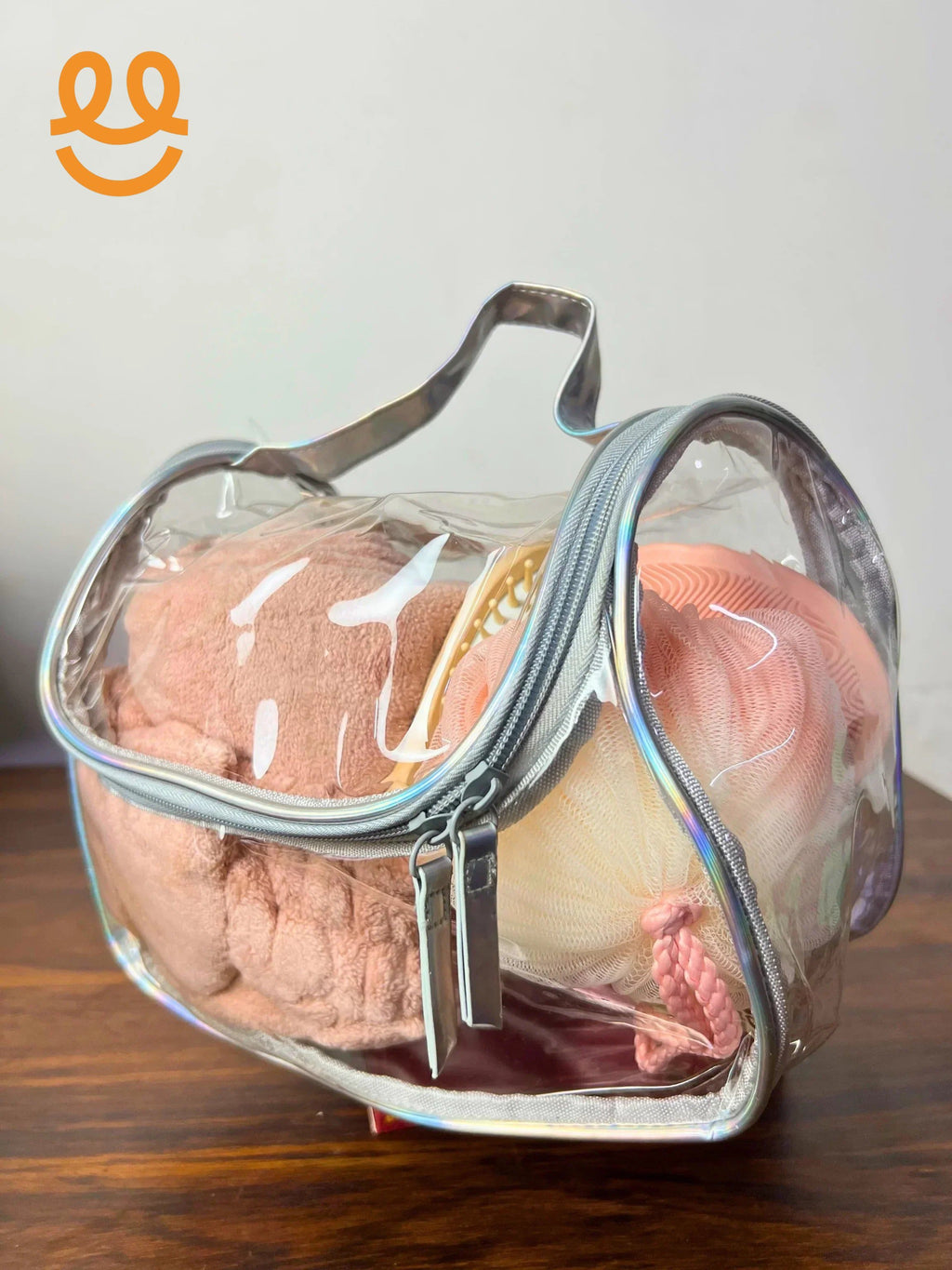 Clear heart-shaped toiletry bag with pink towel, hairbrush, and peach bath pouf inside