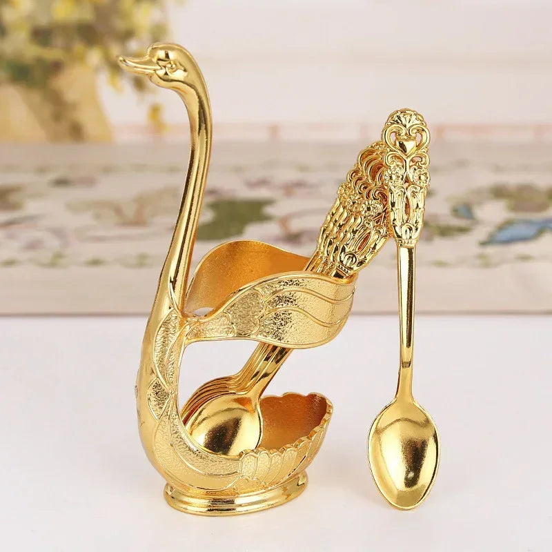 Elegant golden swan-shaped spoon holder with ornate gold teaspoons on white surface