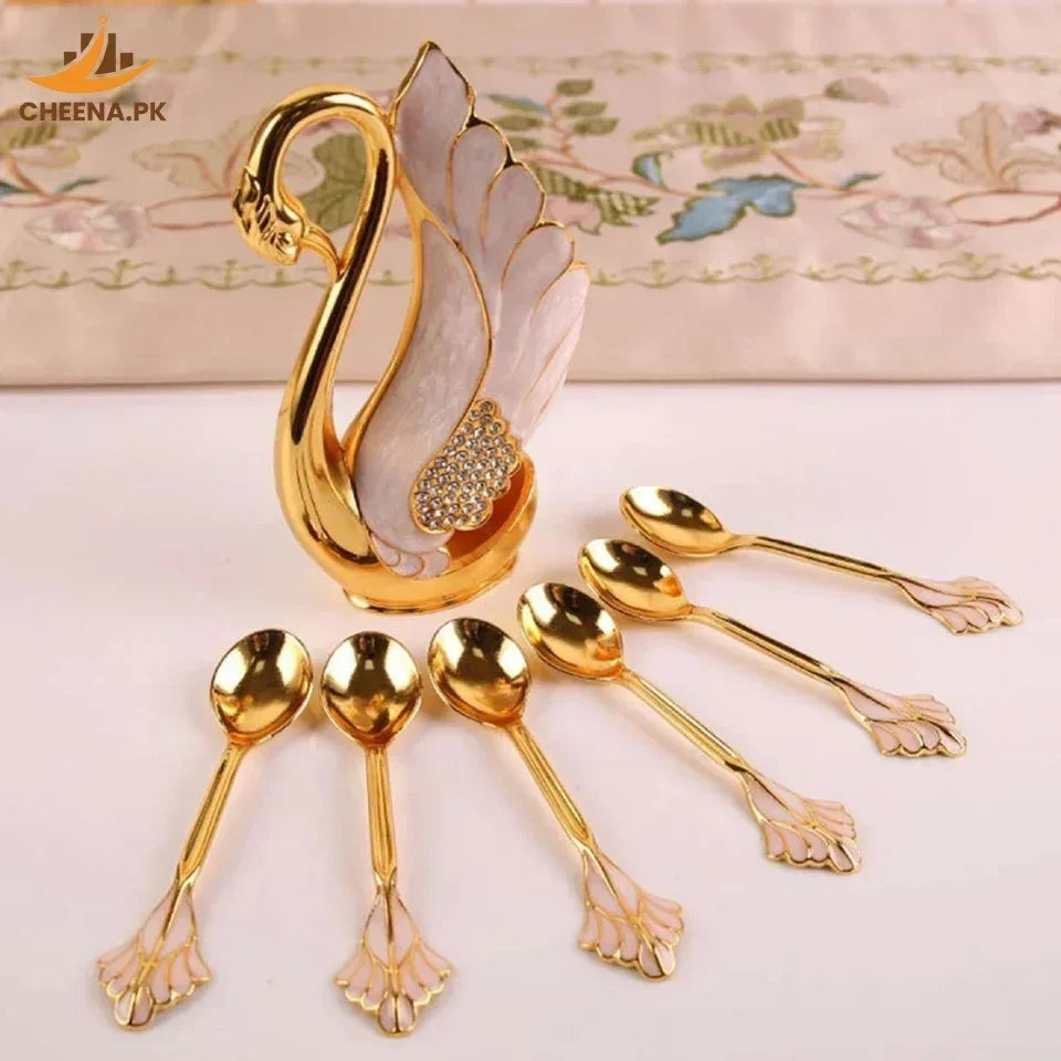 Decorative swan-shaped spoon holder with six gold-plated spoons featuring pink petal-shaped handles on a white surface