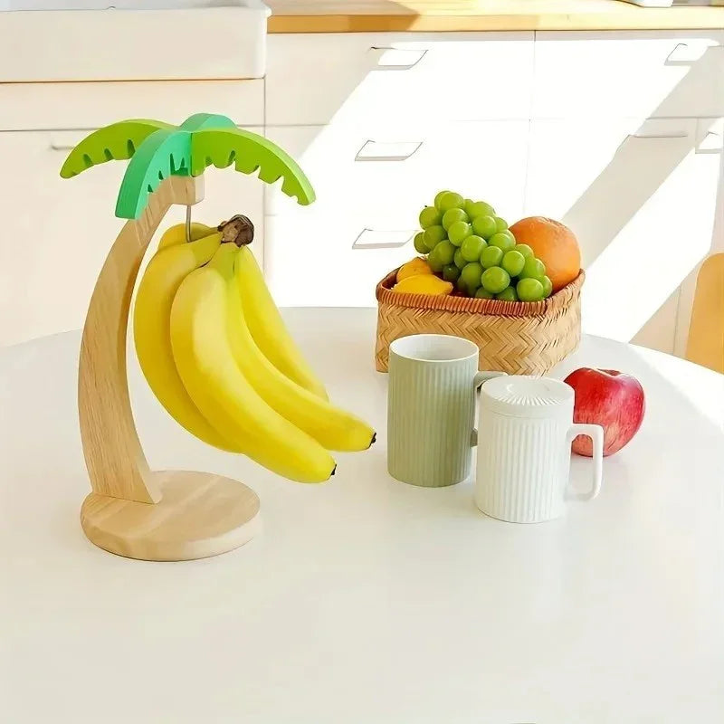 Banana holder shaped like palm tree on white kitchen table with fresh fruit basket and mugs