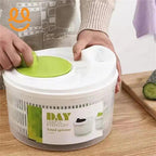 Person using a green and white salad spinner on a wooden kitchen counter with a cutting board and cucumber