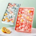 Two trays with round ice cubes containing colorful fruit pieces, lemon halves on white surface