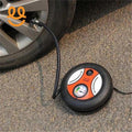 Portable air compressor inflating a car tire on asphalt with pressure gauge and power switch