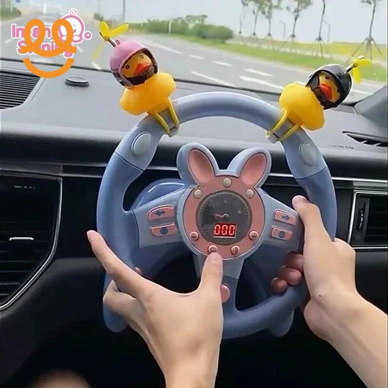 Hands holding a blue toy steering wheel with pink bunny ears and two yellow duck decorations inside a car dashboard