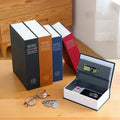 Set of four dictionary-shaped book safes in black, brown, blue, and red on wooden table with glasses and coins