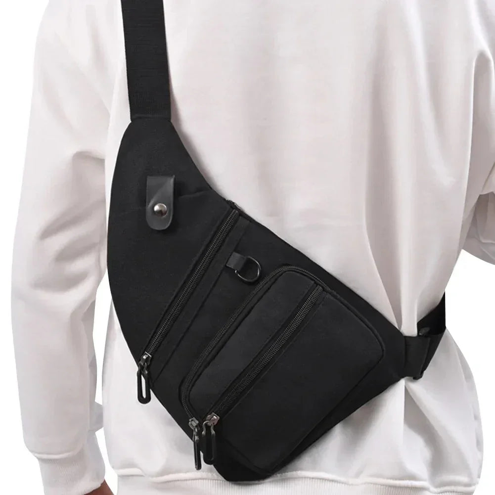 Person wearing black crossbody sling bag with multiple zipper pockets over white sweatshirt