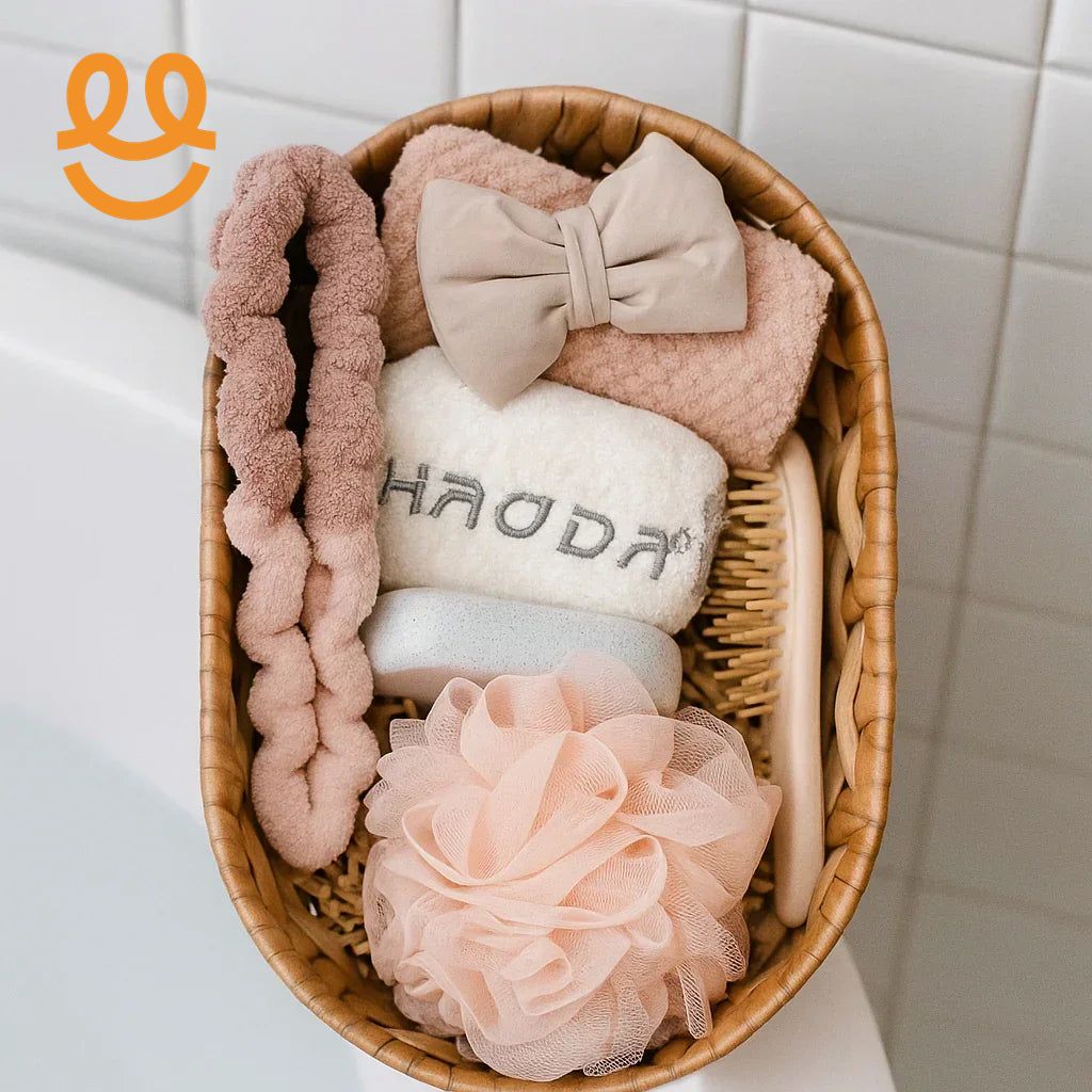Wicker basket with pink bath towel, beige bow, white towel, bath sponge, soap, wooden hairbrush on white tiled bathroom