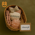 Wicker basket with plush bath accessories including HADDA towel, beige bow, pink scrunchie, brush, and cheena.pk card