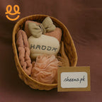 Wicker basket with beige bath accessories including a bow towel, comb, scrunchie, and sponge on brown background