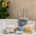 Aesthetic bathroom essentials including a blue shower puff, pumice stone, grey headband, wooden nail brush, and basket on a sink near a faucet