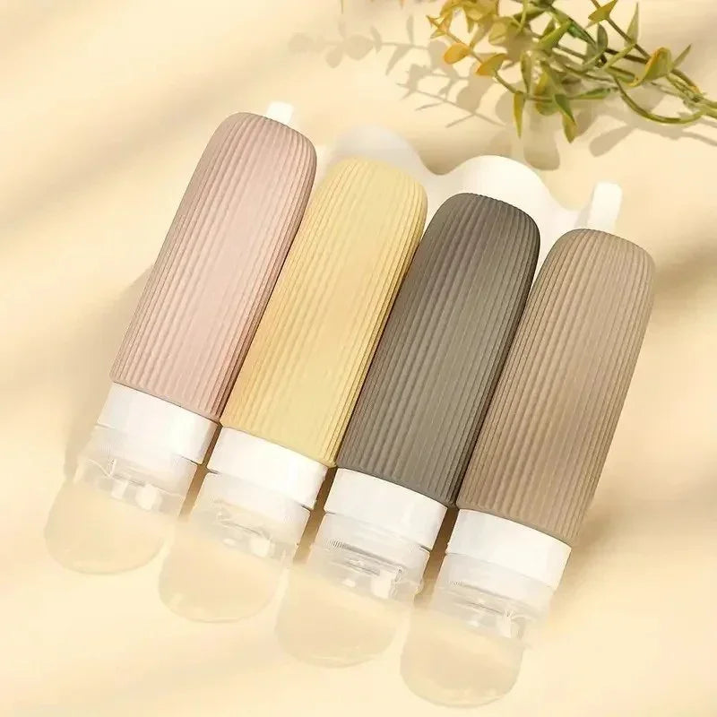 Set of four silicone travel bottles with ribbed texture in pastel and neutral colors on beige background