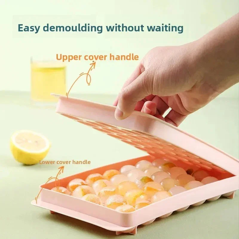 Hand lifting lid of pink silicone mold filled with round citrus fruit ice balls, lemon and juice in background