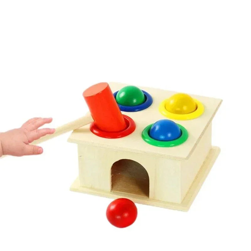 Child playing with wooden ball popper toy, hitting red ball with hammer on colorful pegs