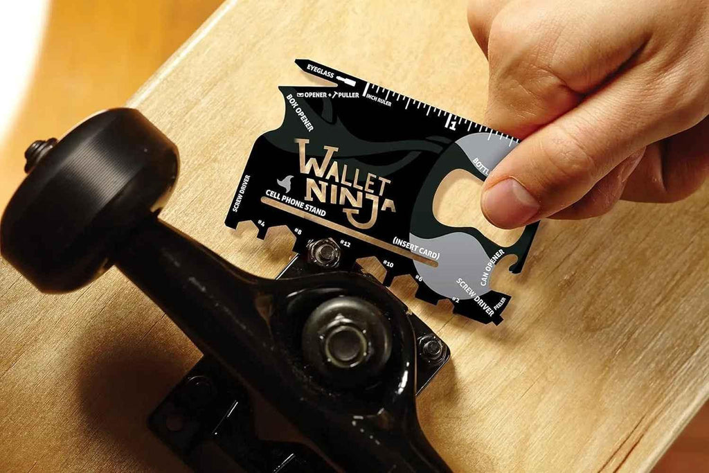 Hand using Wallet Ninja multitool card to tighten skateboard truck on wooden deck