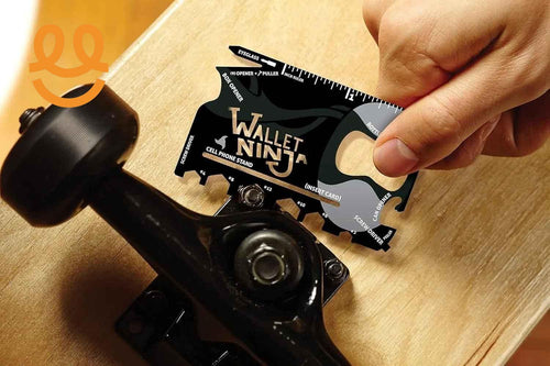 Hand using Wallet Ninja multitool card to tighten skateboard truck on wooden deck