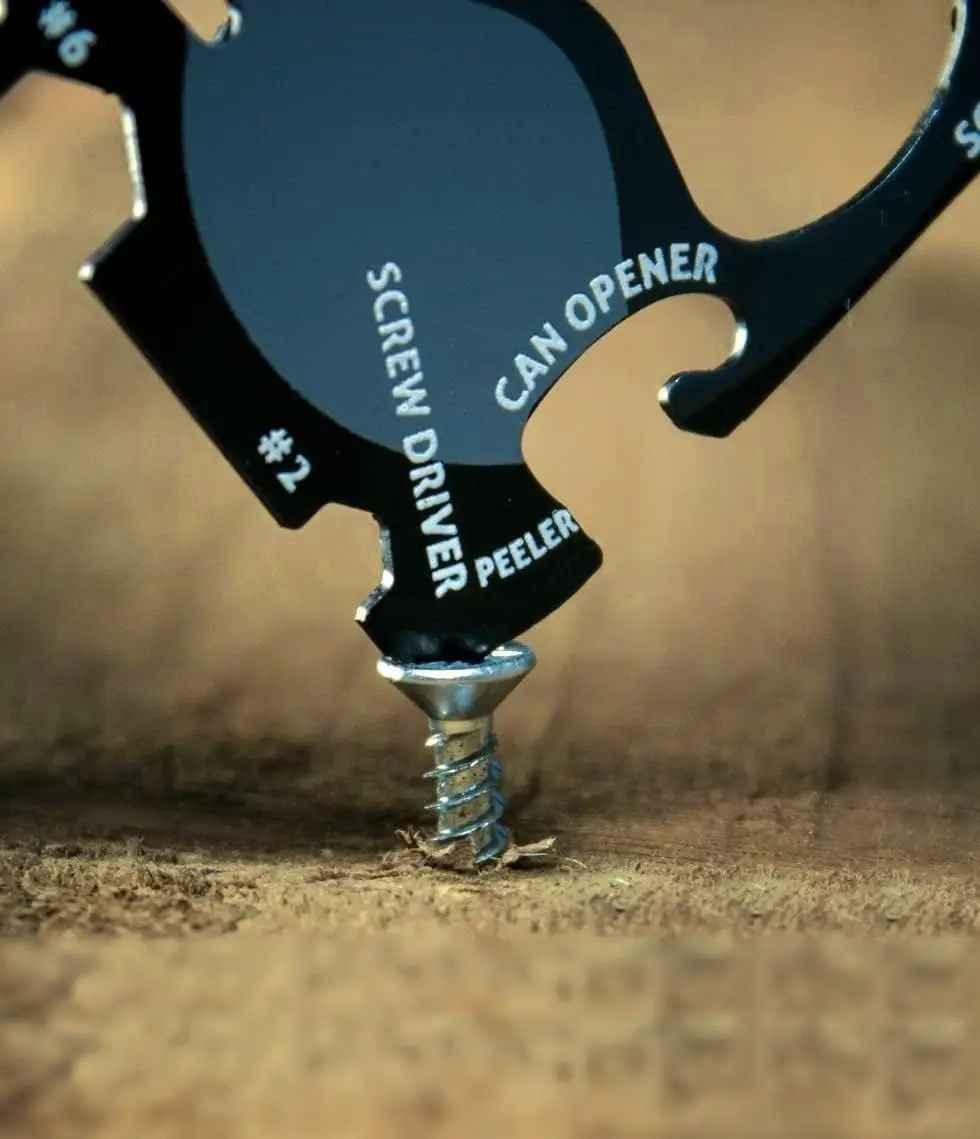 Close-up of a black multi-tool using its screwdriver function to turn a screw in wood