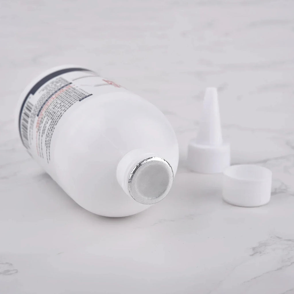 White plastic bottle with foil seal and white nozzle cap parts on marble surface