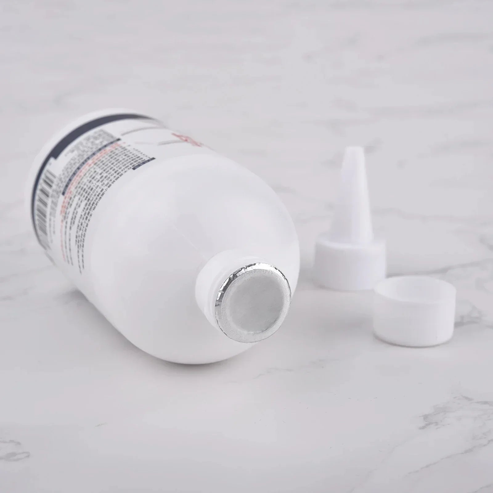 White plastic bottle with foil seal and white nozzle cap parts on marble surface