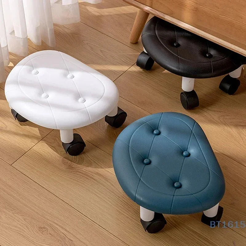 Three small oval rolling stools in white, blue, and black on wooden floor near a wooden desk