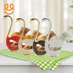 Four swan-shaped decorative holders in red, white, black, and silver with toothpicks on green checkered cloth