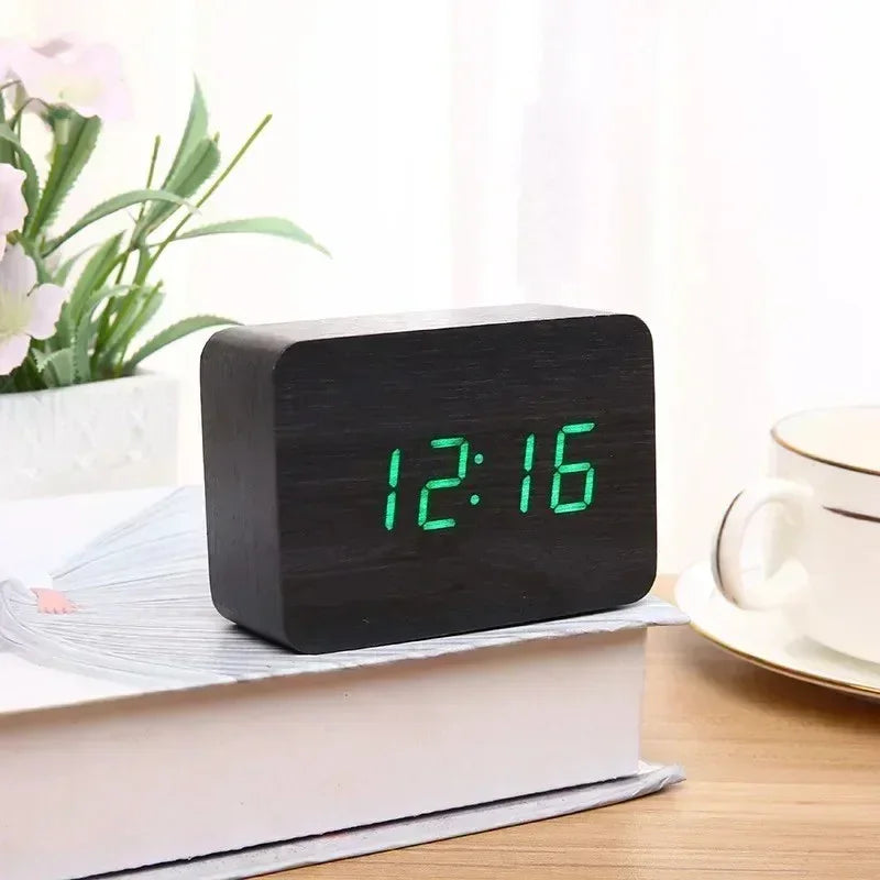 Modern black digital alarm clock with green LED time display on book beside tea cup