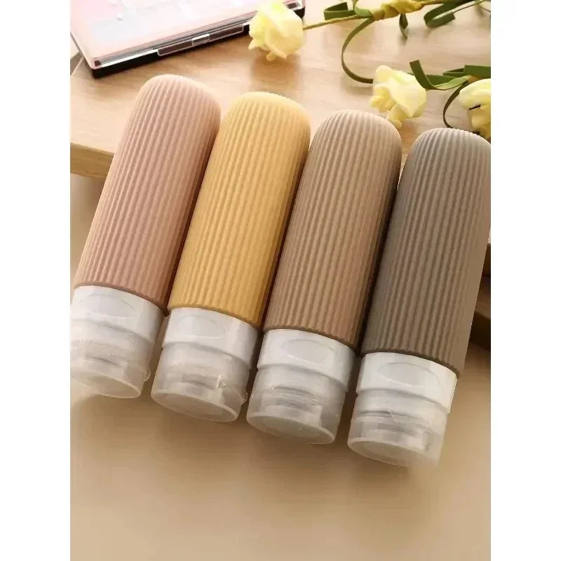 Four travel-sized ribbed silicone squeeze bottles in neutral tones on wooden surface with yellow flowers