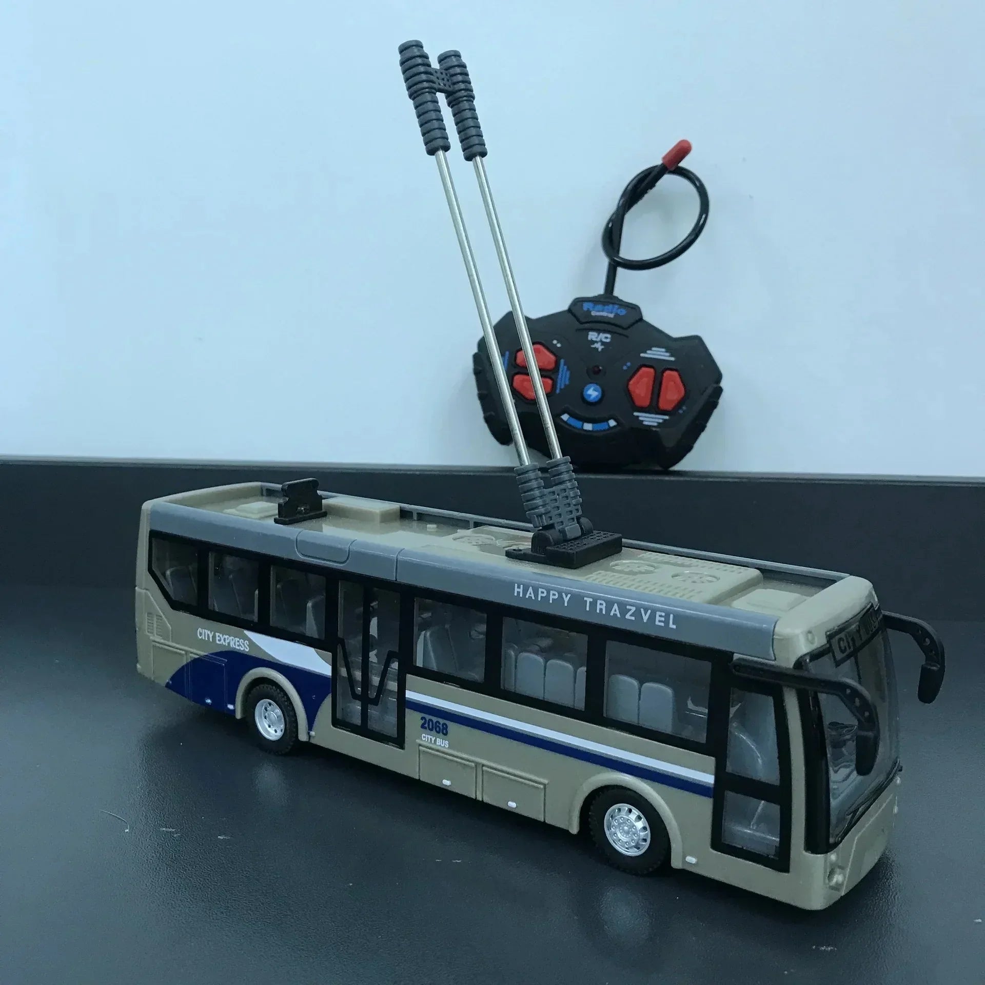 Beige and blue remote control city bus toy with dual antennas and black controller on black surface
