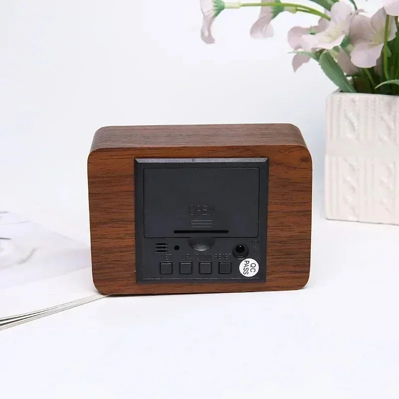 Wooden digital clock with black control panel on white surface next to white flower vase