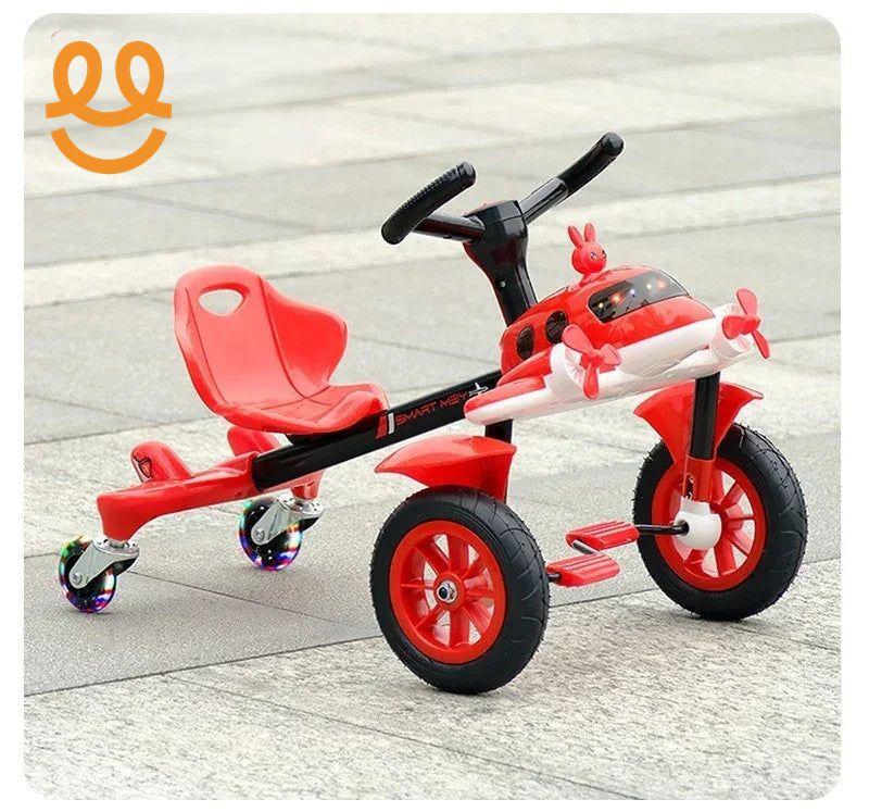 Red children's tricycle with airplane design, front propellers, LED wheel lights, and rear swivel wheels on pavement