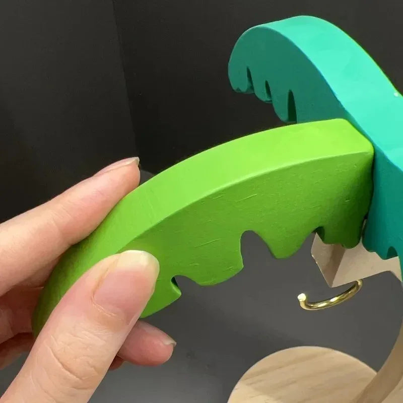 Hand holding green and teal wooden puzzle piece shaped like crocodile jaws on gray background