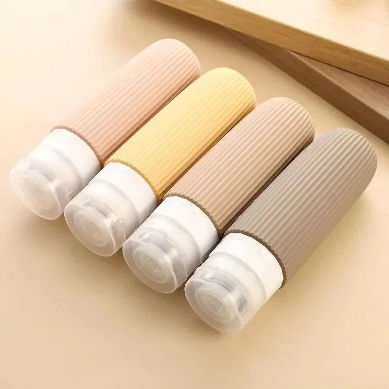 Four pastel-colored silicone travel bottles with clear caps on beige surface