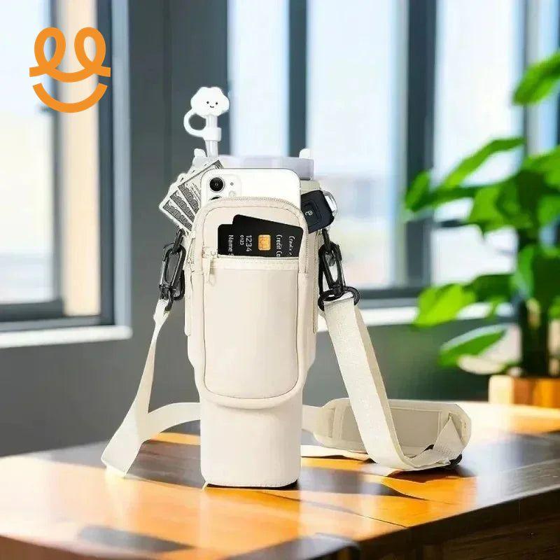 beige crossbody water bottle carrier with front zipper pocket holding phone, credit card, keys, and cash on wooden table