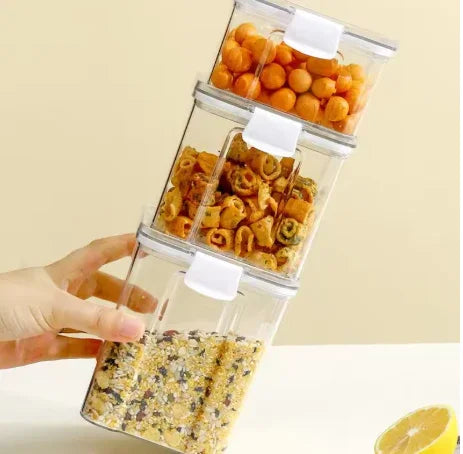 Hand stacking clear plastic snack containers filled with various dry snacks on a beige background