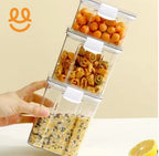 Hand stacking clear plastic snack containers filled with various dry snacks on a beige background