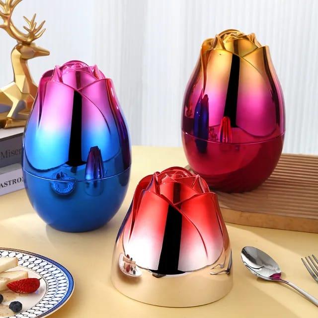Colorful metallic rose-shaped containers in blue, red, and gold on a table with cutlery and a plate