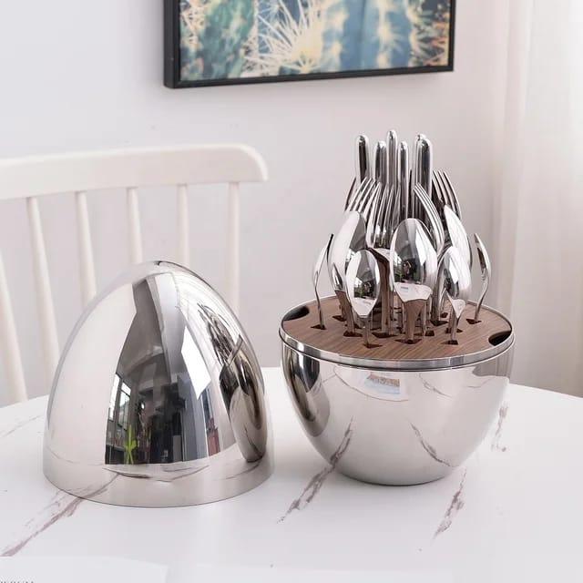 Modern stainless steel cutlery set with forks, spoons, and knives in a sleek round holder on a marble table