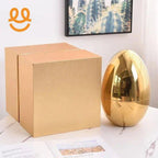 Gold decorative egg and two gold gift boxes on white marble table under cactus wall art