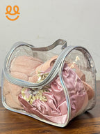 Clear cosmetic bag with silver trim containing pink velvet scrunchies and a pink towel on wooden surface