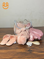 Transparent cosmetic bag with pink spa items including slippers, bathrobe, shower cap, loofah, hair brush, and pumice stone