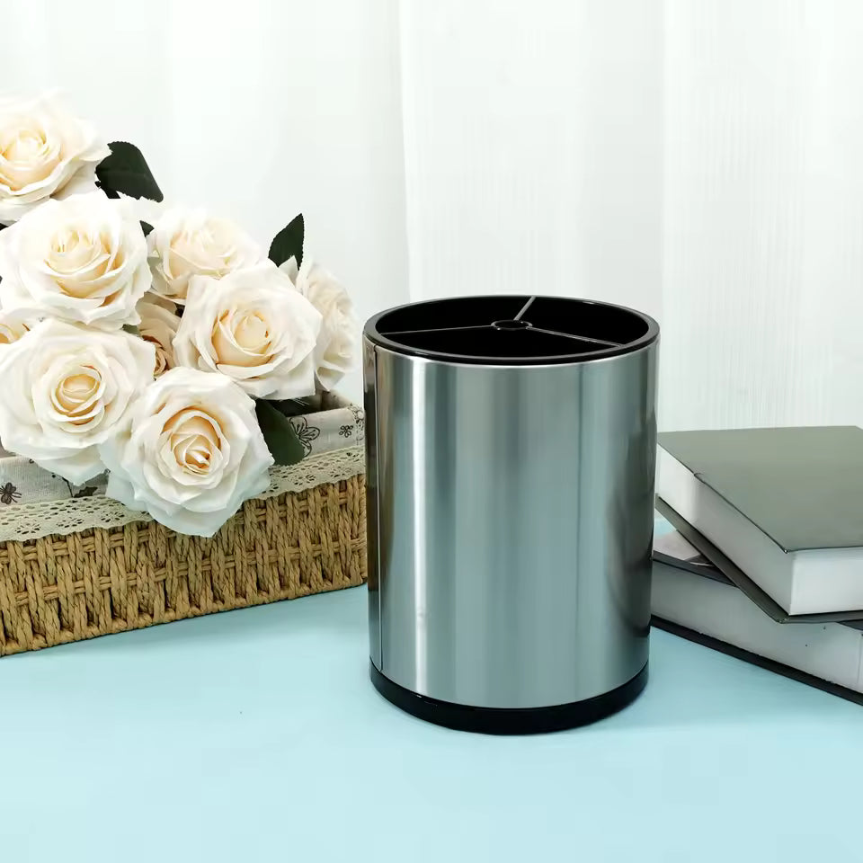 Stainless steel pen holder on blue surface with white roses in wicker basket and stacked books