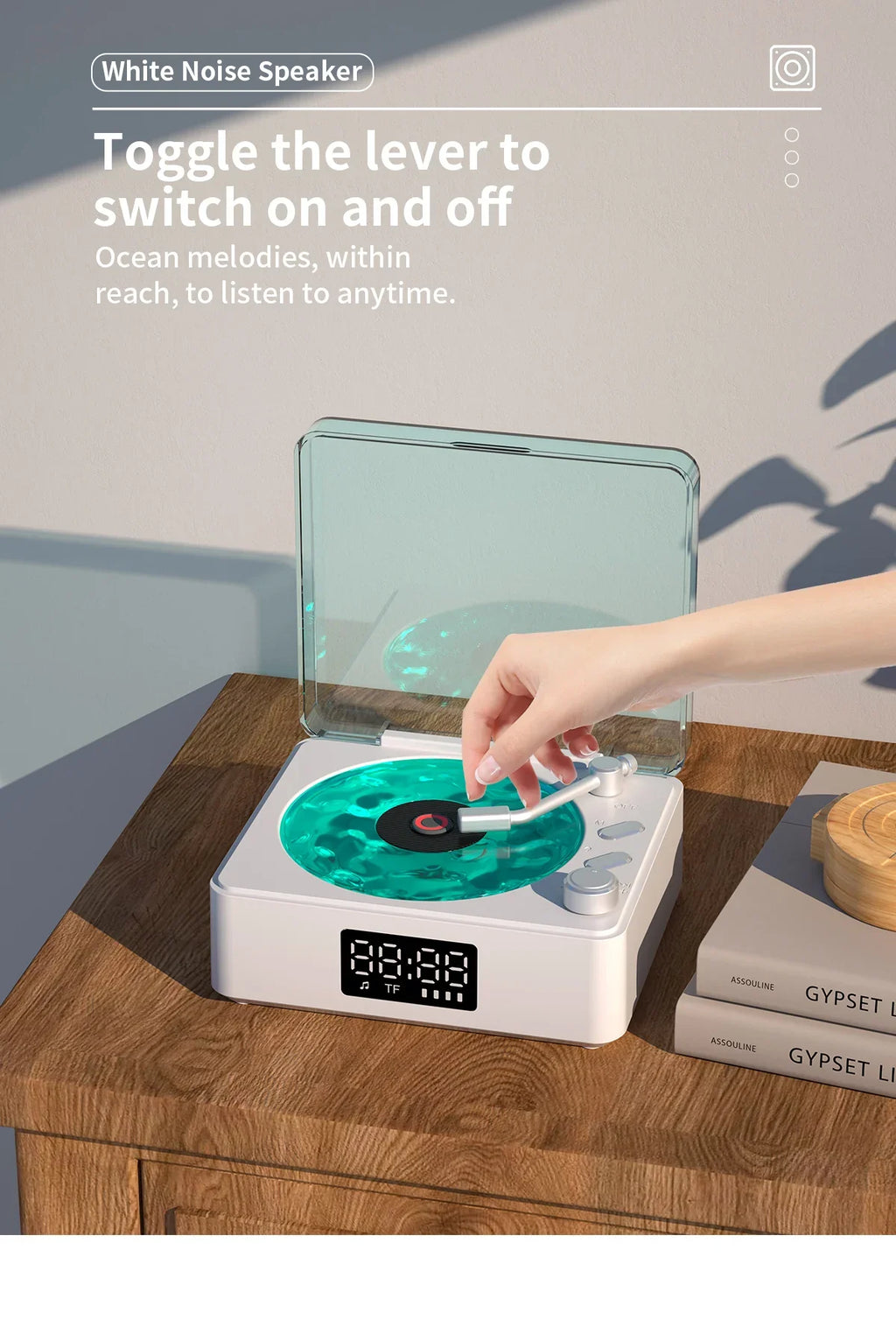 Hand toggling white noise speaker shaped like a teal vinyl record player on wooden table with books