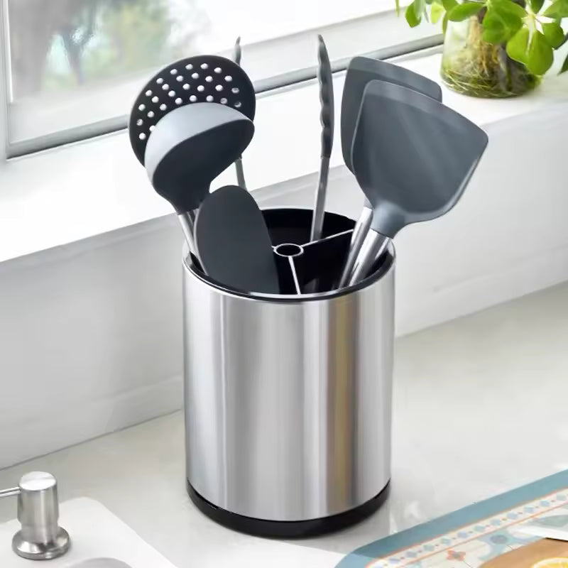 Stainless steel kitchen utensil holder with black silicone cooking tools on a countertop near window