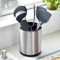 Stainless steel kitchen utensil holder with black silicone cooking tools on a countertop near window