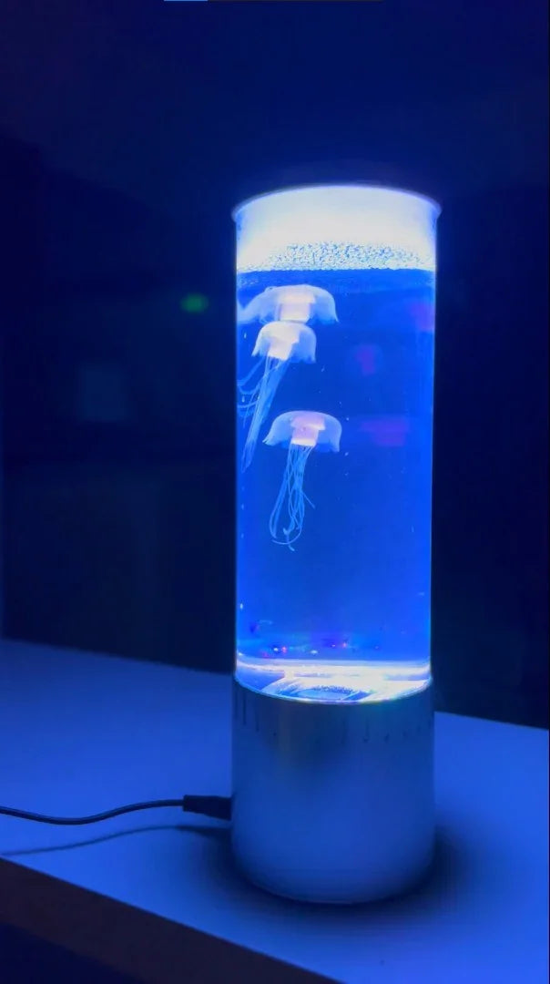 Glowing blue jellyfish lamp on table with three illuminated jellyfish inside cylindrical tank