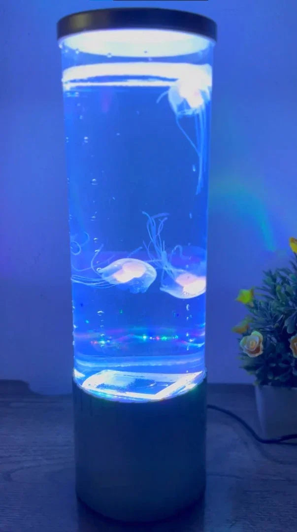 Modern cylindrical aquarium lamp with glowing artificial jellyfish in blue light on wooden surface