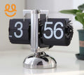 Retro black flip clock showing 3:56 PM with metallic base on white surface and plant in background